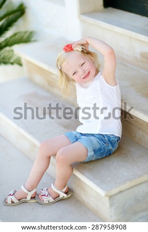 Adorable little girl sitting on stairs on warm and sunny summer day in typical italian town
