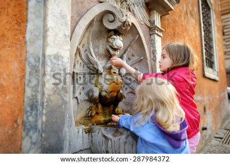 Two sisters having fun with drinking water fountain in Italy on warm and sunny summer day in Rome