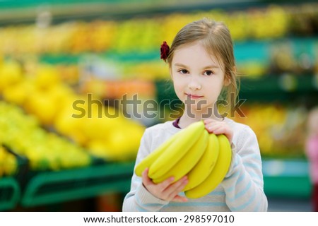 Cute little girl holding bananas in a food store or supermarket