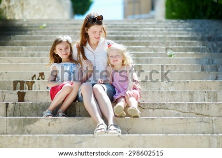 Two adorable little sisters and their mom having fun together on warm and sunny summer day in italian town