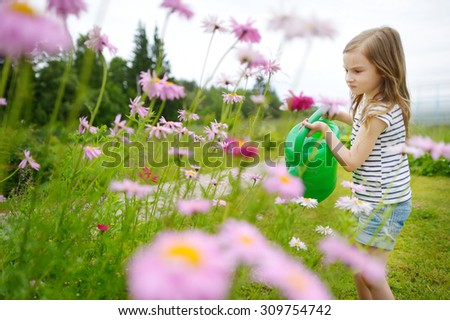 Adorable little preschooler girl watering flowers and plants in the garden