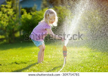 Adorable little girl playing with a sprinkler in a backyard on sunny summer day