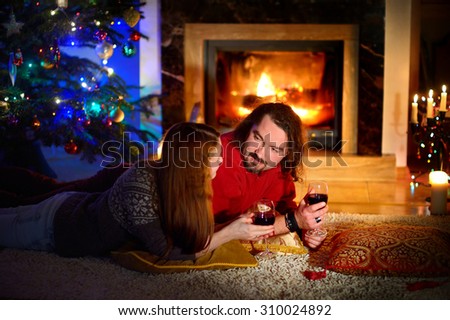 Happy couple laying by a fireplace in a cozy dark living room on Christmas eve