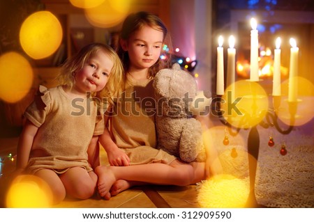 Happy little girls sitting by a fireplace in a cozy dark living room on Christmas eve