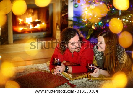 Happy couple laying by a fireplace in a cozy dark living room on Christmas eve