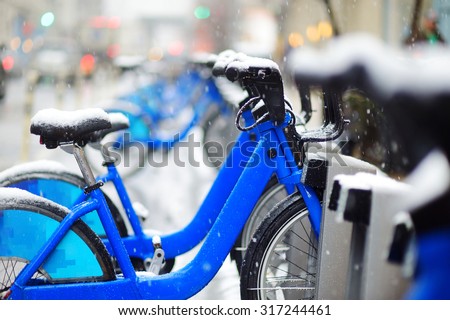 Row of rental city bikes at docking station covered with snow in New York at winter