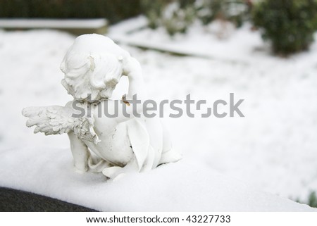 Angel statue on a cemetery with snow looking to the graves.