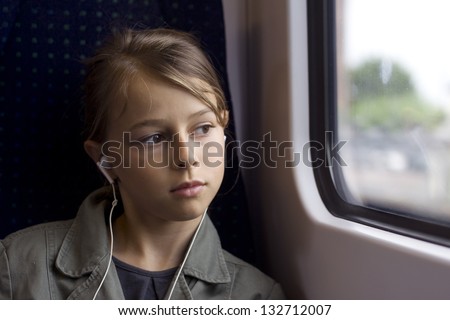 Young girl with headphones looking out of a train window