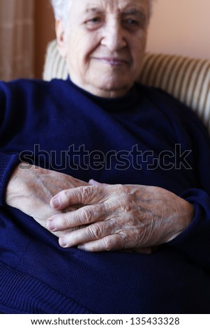 close up wrinkled hands of a senior person resting in an armchair