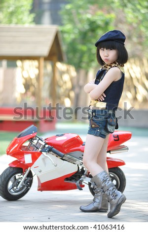 Adorable little girl standing by the red toy motorbike.