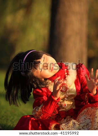 The complacent little Chinese girl in red is sitting on the grassland enjoy herself.