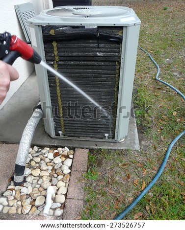 Man spraying insect repellant on evaporator coils to prevent nesting and feeding ants from damaging the contactor of air conditioner heat pump unit.