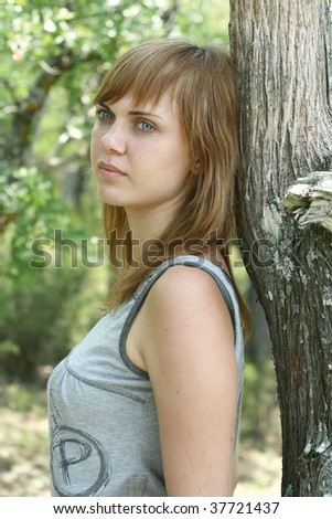 The young nice girl at a tree in wood. She looks afar and dreams.
