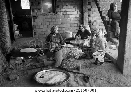 EVRENLERYAVSI,  TURKEY - JUNE 24, 2014: Village women prepare traditional flatbread on an open fire. Black and white