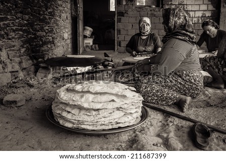 EVRENLERYAVSI, TURKEY - JUNE 24, 2014: Village women prepare traditional flatbread on an open fire. Sepia