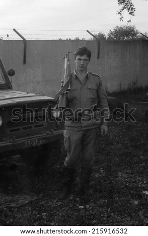 MOSCOW REGION, RUSSIA - CIRCA 1993: A soldier with a gun standing near army SUV UAZ-469. Film scan. Large grain, circa 1993
