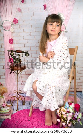 Cute little girl with old phone wrapped in a delicate blanket sitting on a wooden studio in the scenery