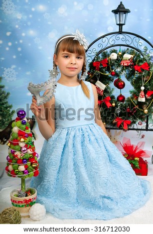 cute little girl in a blue dress with a carnival mask on a Christmas background