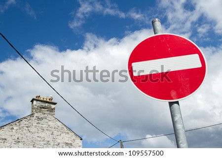 A no entry sign with a red circle and white bar on a metal post against a blue sky with cloud.