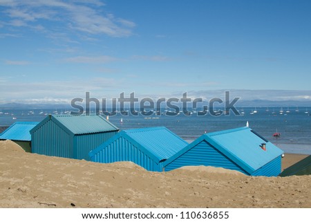 Blue beach huts in the sand look out over the sea with yachts and mountains in the distance at Abersoch, Gwynedd, Wales, UK.
