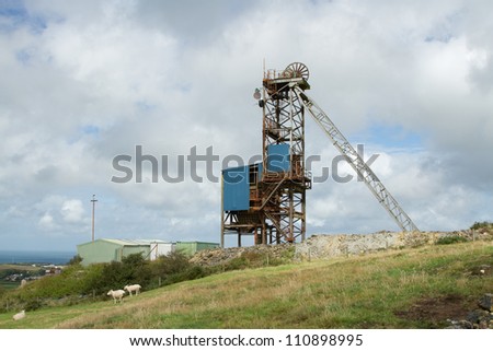 A winding gear tower structure at a minehead with wheel and support against a cloudy sky.