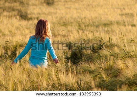 Cute happy girl walking in the field of wheat on sunny spring day.