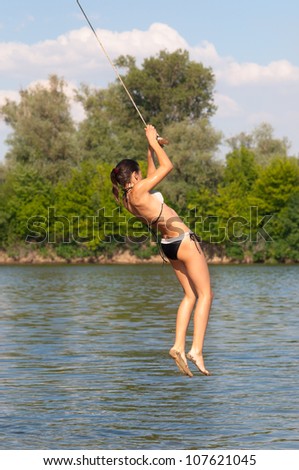 Teenage girl jumping in the river from the swinging rope on sunny summer day.