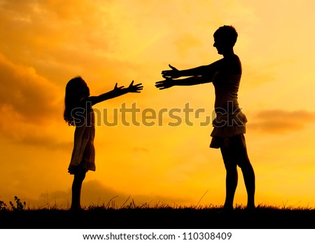 Silhouettes of mother and daughter meeting on the meadow at summer sunset.
