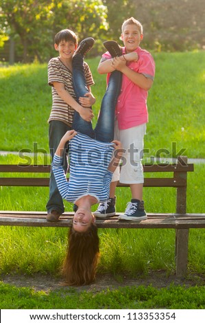 Teenage boys holding their girl friend upside down in the park on beautiful spring day.
