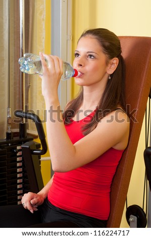 Beautiful girl drinking water after hard exercise in fitness center.