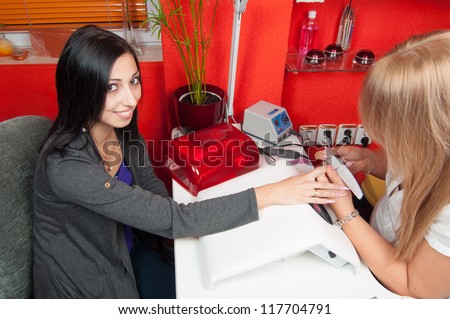 Manicure process in beauty salon showing smiling girl during nail cleaning and polishing.