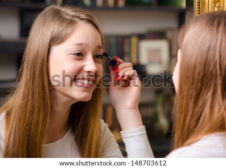 Beautiful teenage girl having fun while putting make up in front of the old mirror.