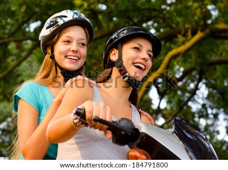 Two teenage girlfriends riding scooter on sunny summer day.