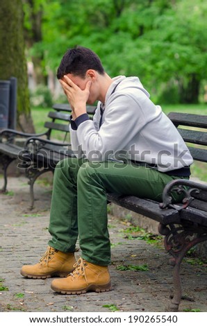 Troubled young man sitting in the park on beautiful spring day.