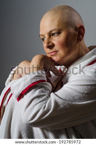 Bald woman suffering from cancer sitting lost in thoughts.
