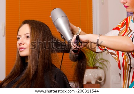 Hairdresser making hair of beautiful happy girl in beauty salon.