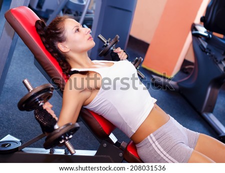 Beautiful girl lifting weights in the modern gym.