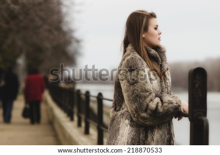 Portrait of the glamorous brunette lady in expensive fur coat watching river.
