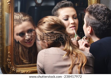 Beautiful girls having fun while putting make up in front of the old mirror.