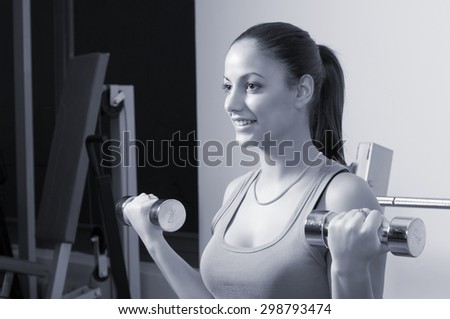 Young happy fitness girl exercising with dumbbells in modern gym.