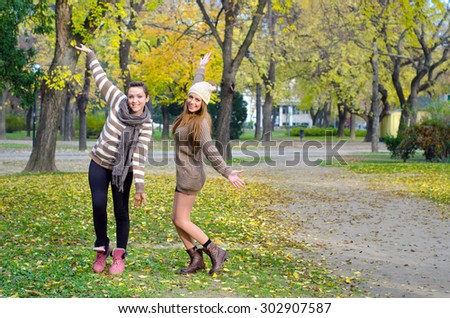Two beautiful girlfriends having fun in the park on colorful autumn day.