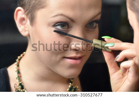 Beautiful young woman having fun while putting make up in front of the old mirror.