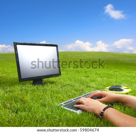 Working on the computer in the middle of the beautiful green meadow and under the blue sky on the sunny summer day.
