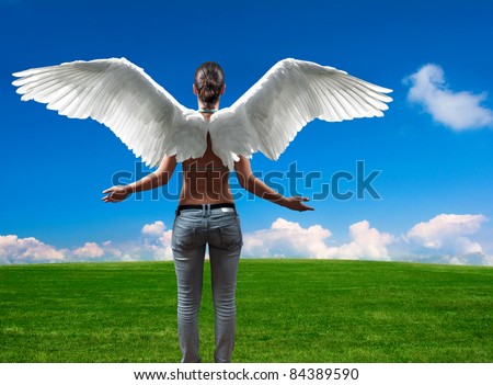 Girl with angel wings standing in front of the open empty meadow and blue sky full of white clouds at the horizon.