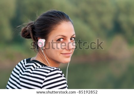 Pretty smiling teenage girl listens to music while enjoying autumn nature.