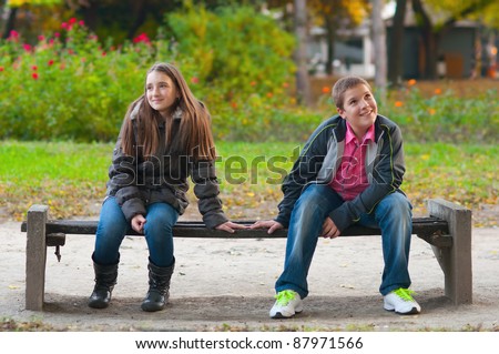 Shy boy and the girl sitting in the park and lightly touching each other finger tips.