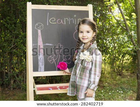 little girl drawing on blackboard in nature, learning and have a lot of fun