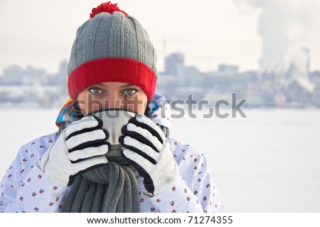 Beautiful woman drinking hot tea on a frozen river on the background of the city. Winter landscape.