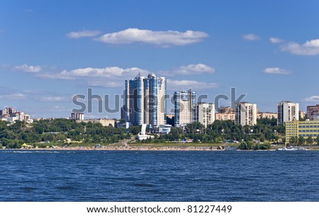 High apartment buildings on the quay. Beach filled with people. Summer urban landscape with a river. Samara. Russia.