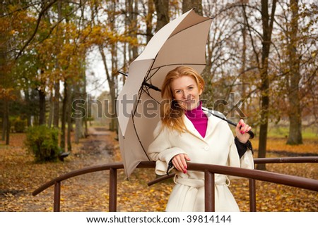 Young smiling  redhead woman with umbrela during fall on a bridge